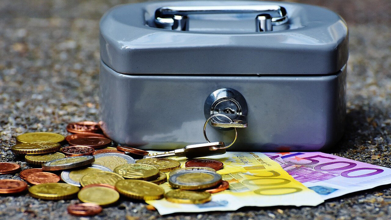 Geldkasse mit Schlüssel, davor liegen Euro-Scheine und Euro-Münzen / Cash box with key, euro notes and coins in front of it